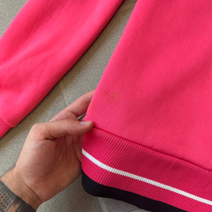 Nike Pink Women's Bomber-style Zip-up features a pink, heavyweight cotton construction with a tall black collar. It has a full front zipper with a circular zipper pull and two front Velcro pockets, one with a small Nike tag. The garment has a jacket-style construction.
