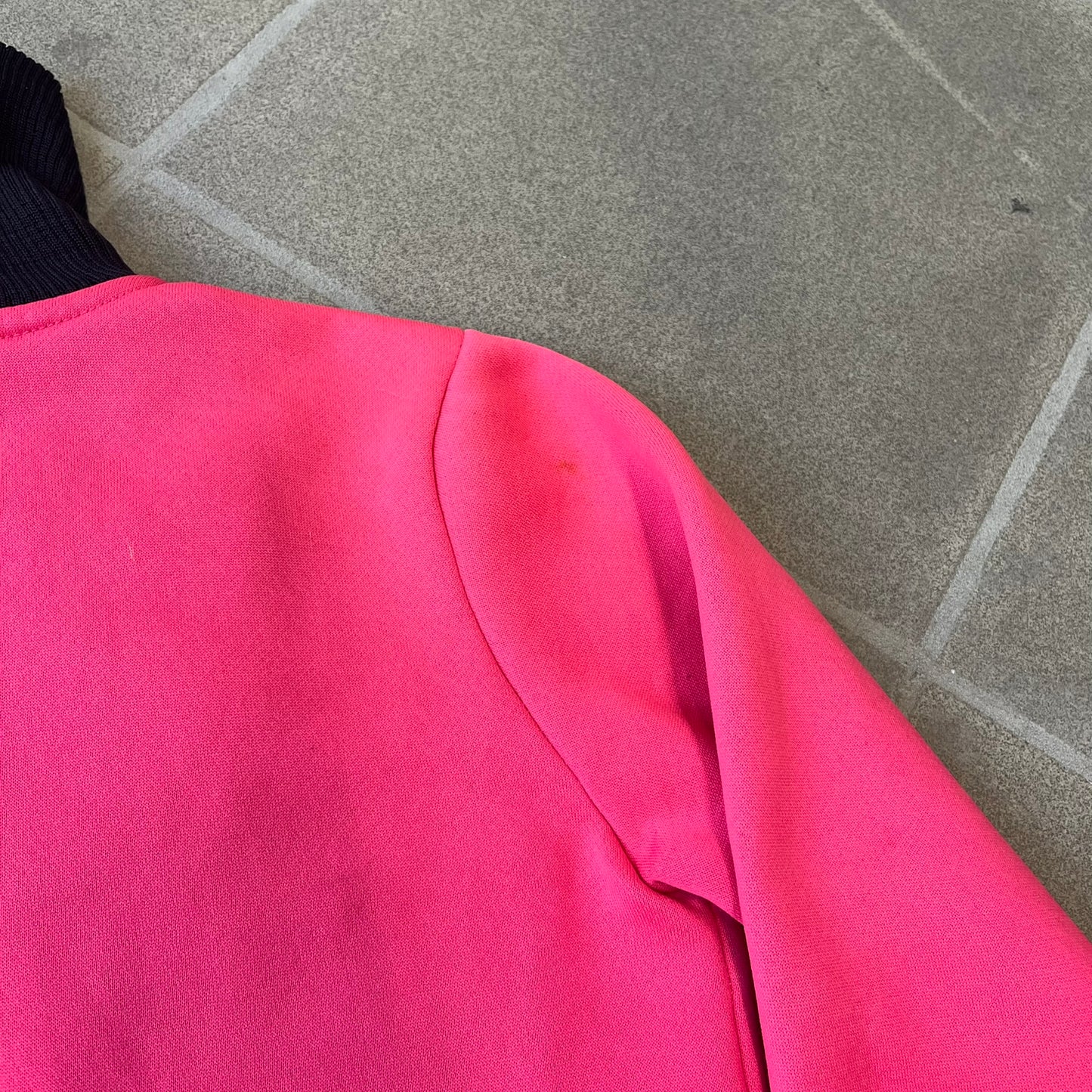 Nike Pink Women's Bomber-style Zip-up features a pink, heavyweight cotton construction with a tall black collar. It has a full front zipper with a circular zipper pull and two front Velcro pockets, one with a small Nike tag. The garment has a jacket-style construction.
