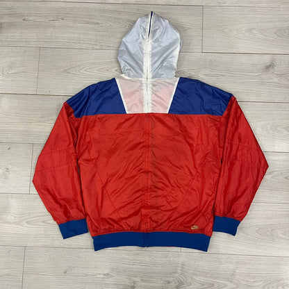 Nike Red/Blue/White Split Windbreaker featuring a modular design with front and back zippers that allow attachment to compatible jackets. The layout includes dominant red panels across the sleeves and upper front, contrasted with blue accents, a white hood, and a blue-white-black camo hood lining. Finished with a gold embroidered Nike logo on the chest.