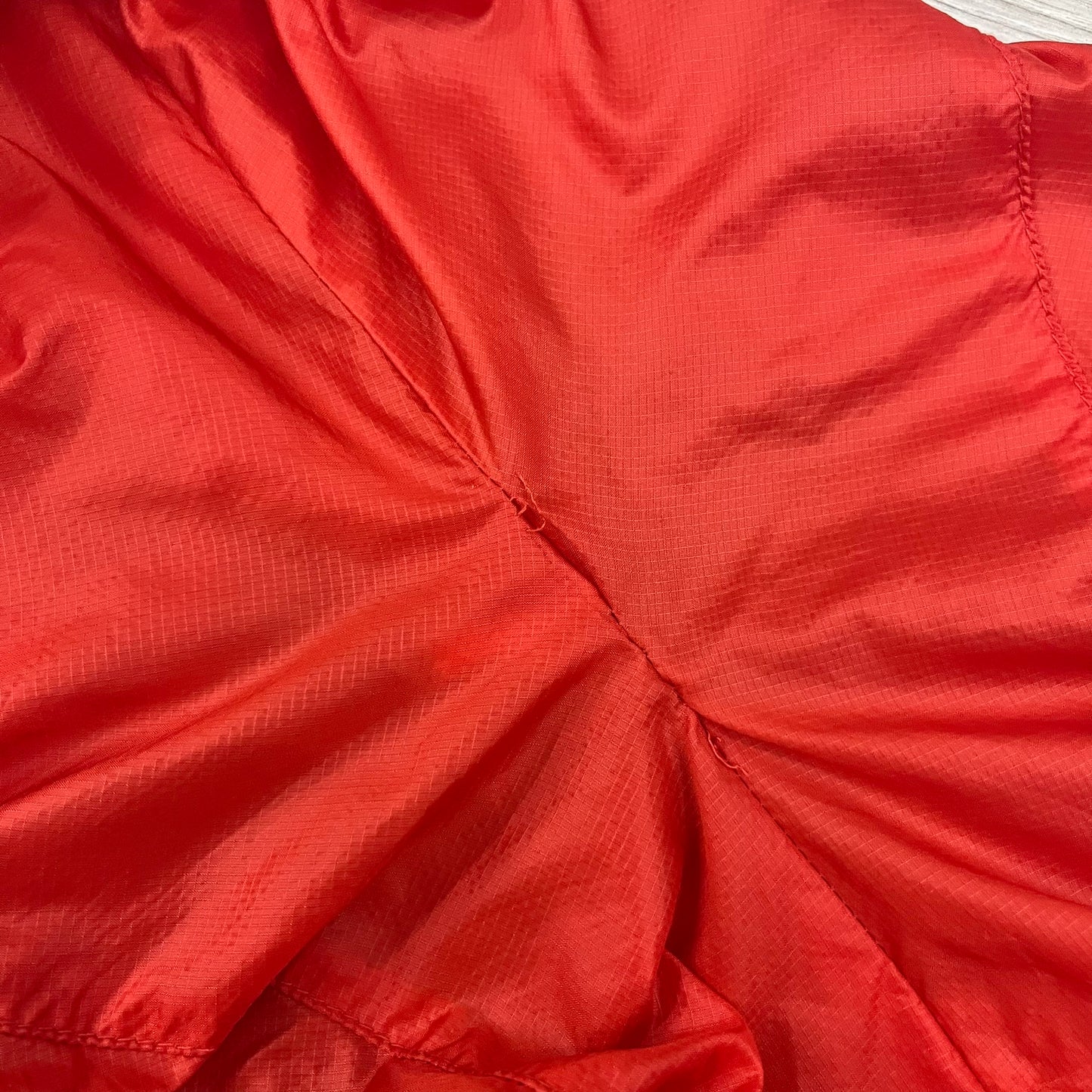 Nike Red/Blue/White Split Windbreaker featuring a modular design with front and back zippers that allow attachment to compatible jackets. The layout includes dominant red panels across the sleeves and upper front, contrasted with blue accents, a white hood, and a blue-white-black camo hood lining. Finished with a gold embroidered Nike logo on the chest.