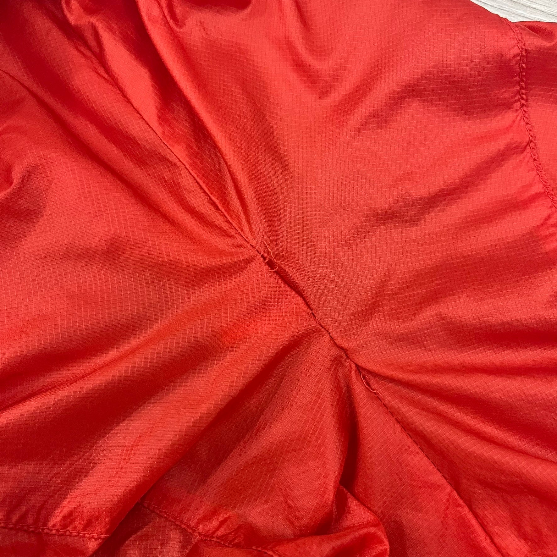 Nike Red/Blue/White Split Windbreaker featuring a modular design with front and back zippers that allow attachment to compatible jackets. The layout includes dominant red panels across the sleeves and upper front, contrasted with blue accents, a white hood, and a blue-white-black camo hood lining. Finished with a gold embroidered Nike logo on the chest.