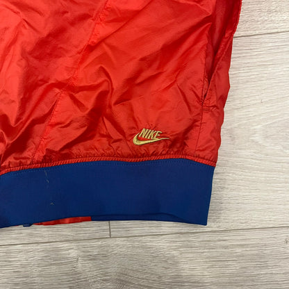 Nike Red/Blue/White Split Windbreaker featuring a modular design with front and back zippers that allow attachment to compatible jackets. The layout includes dominant red panels across the sleeves and upper front, contrasted with blue accents, a white hood, and a blue-white-black camo hood lining. Finished with a gold embroidered Nike logo on the chest.
