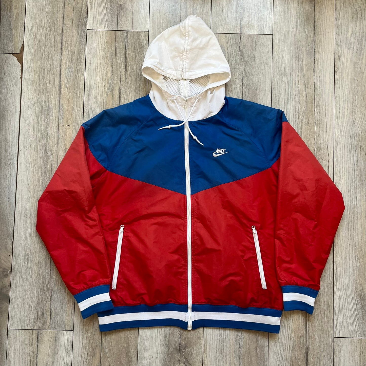 Nike Russia Olympics Split Windbreaker from 2008, created by designer Jarrett Reynolds. Crafted in a red, blue and white color wave. White Nike embroidery swoosh on the left side of the chest. The upper half of the jacket is blue with white hood, and the bottom is red with white accents. This innovative jacket can be zipped apart on both sides and merged with other compatible models. Hidden inside, a small Russia flags accent completes the concept.