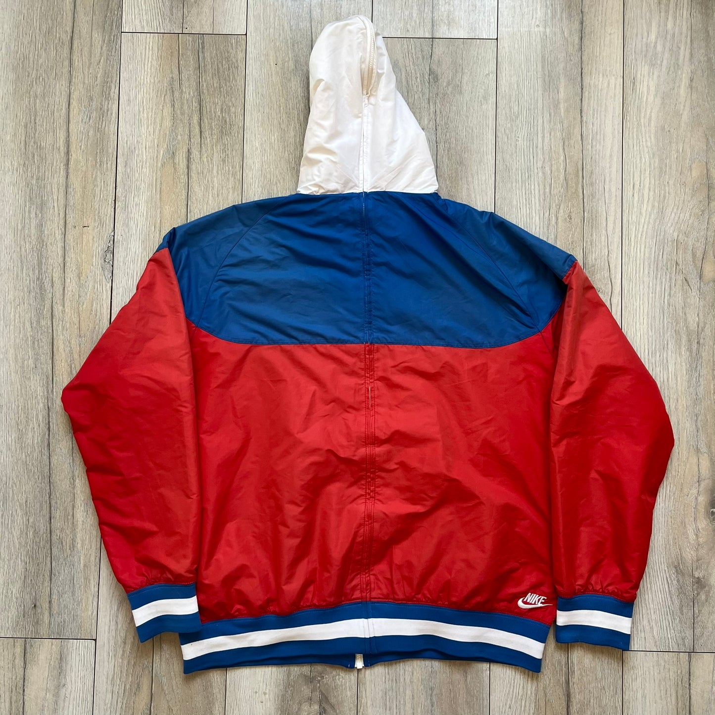 Nike Russia Olympics Split Windbreaker from 2008, created by designer Jarrett Reynolds. Crafted in a red, blue and white color wave. White Nike embroidery swoosh on the left side of the chest. The upper half of the jacket is blue with white hood, and the bottom is red with white accents. This innovative jacket can be zipped apart on both sides and merged with other compatible models. Hidden inside, a small Russia flags accent completes the concept.
