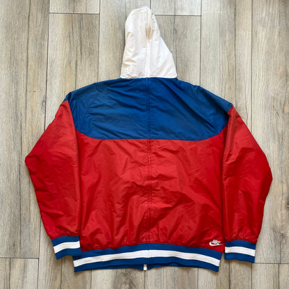 Nike Russia Olympics Split Windbreaker from 2008, created by designer Jarrett Reynolds. Crafted in a red, blue and white color wave. White Nike embroidery swoosh on the left side of the chest. The upper half of the jacket is blue with white hood, and the bottom is red with white accents. This innovative jacket can be zipped apart on both sides and merged with other compatible models. Hidden inside, a small Russia flags accent completes the concept.