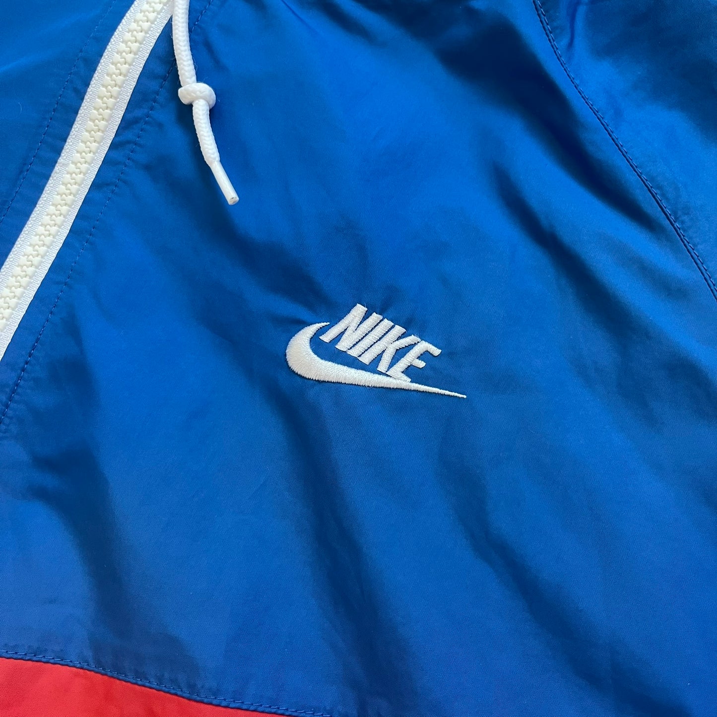 Nike Russia Olympics Split Windbreaker from 2008, created by designer Jarrett Reynolds. Crafted in a red, blue and white color wave. White Nike embroidery swoosh on the left side of the chest. The upper half of the jacket is blue with white hood, and the bottom is red with white accents. This innovative jacket can be zipped apart on both sides and merged with other compatible models. Hidden inside, a small Russia flags accent completes the concept.