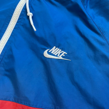 Nike Russia Olympics Split Windbreaker from 2008, created by designer Jarrett Reynolds. Crafted in a red, blue and white color wave. White Nike embroidery swoosh on the left side of the chest. The upper half of the jacket is blue with white hood, and the bottom is red with white accents. This innovative jacket can be zipped apart on both sides and merged with other compatible models. Hidden inside, a small Russia flags accent completes the concept.