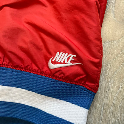 Nike Russia Olympics Split Windbreaker from 2008, created by designer Jarrett Reynolds. Crafted in a red, blue and white color wave. White Nike embroidery swoosh on the left side of the chest. The upper half of the jacket is blue with white hood, and the bottom is red with white accents. This innovative jacket can be zipped apart on both sides and merged with other compatible models. Hidden inside, a small Russia flags accent completes the concept.