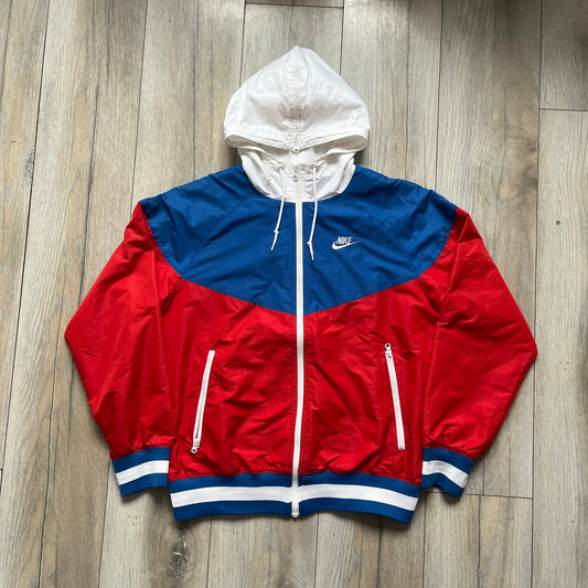 Nike Russia Olympics Split Windbreaker from 2008, created by designer Jarrett Reynolds. Crafted in a red, blue and white color wave. White Nike embroidery swoosh on the left side of the chest. The upper half of the jacket is blue with white hood, and the bottom is red with white accents. This innovative jacket can be zipped apart on both sides and merged with other compatible models. Hidden inside, a small Russia flags accent completes the concept.