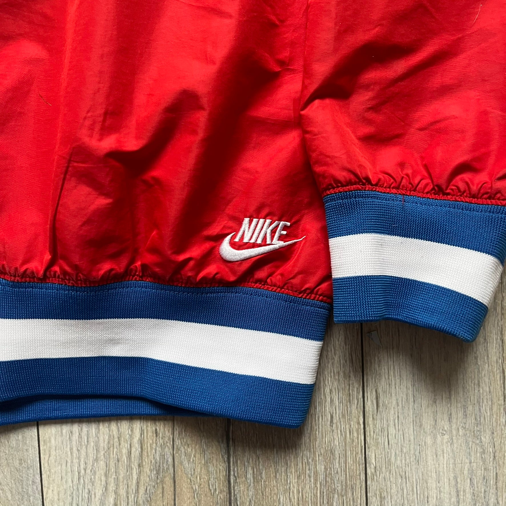 Nike Russia Olympics Split Windbreaker from 2008, created by designer Jarrett Reynolds. Crafted in a red, blue and white color wave. White Nike embroidery swoosh on the left side of the chest. The upper half of the jacket is blue with white hood, and the bottom is red with white accents. This innovative jacket can be zipped apart on both sides and merged with other compatible models. Hidden inside, a small Russia flags accent completes the concept.