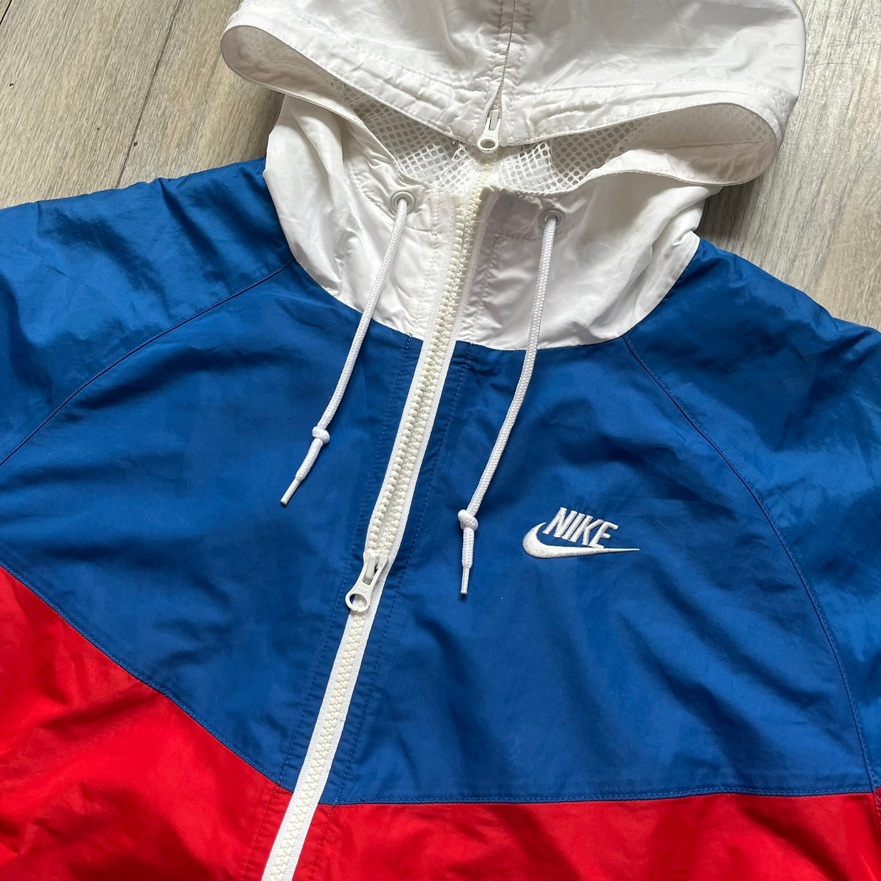 Nike Russia Olympics Split Windbreaker from 2008, created by designer Jarrett Reynolds. Crafted in a red, blue and white color wave. White Nike embroidery swoosh on the left side of the chest. The upper half of the jacket is blue with white hood, and the bottom is red with white accents. This innovative jacket can be zipped apart on both sides and merged with other compatible models. Hidden inside, a small Russia flags accent completes the concept.