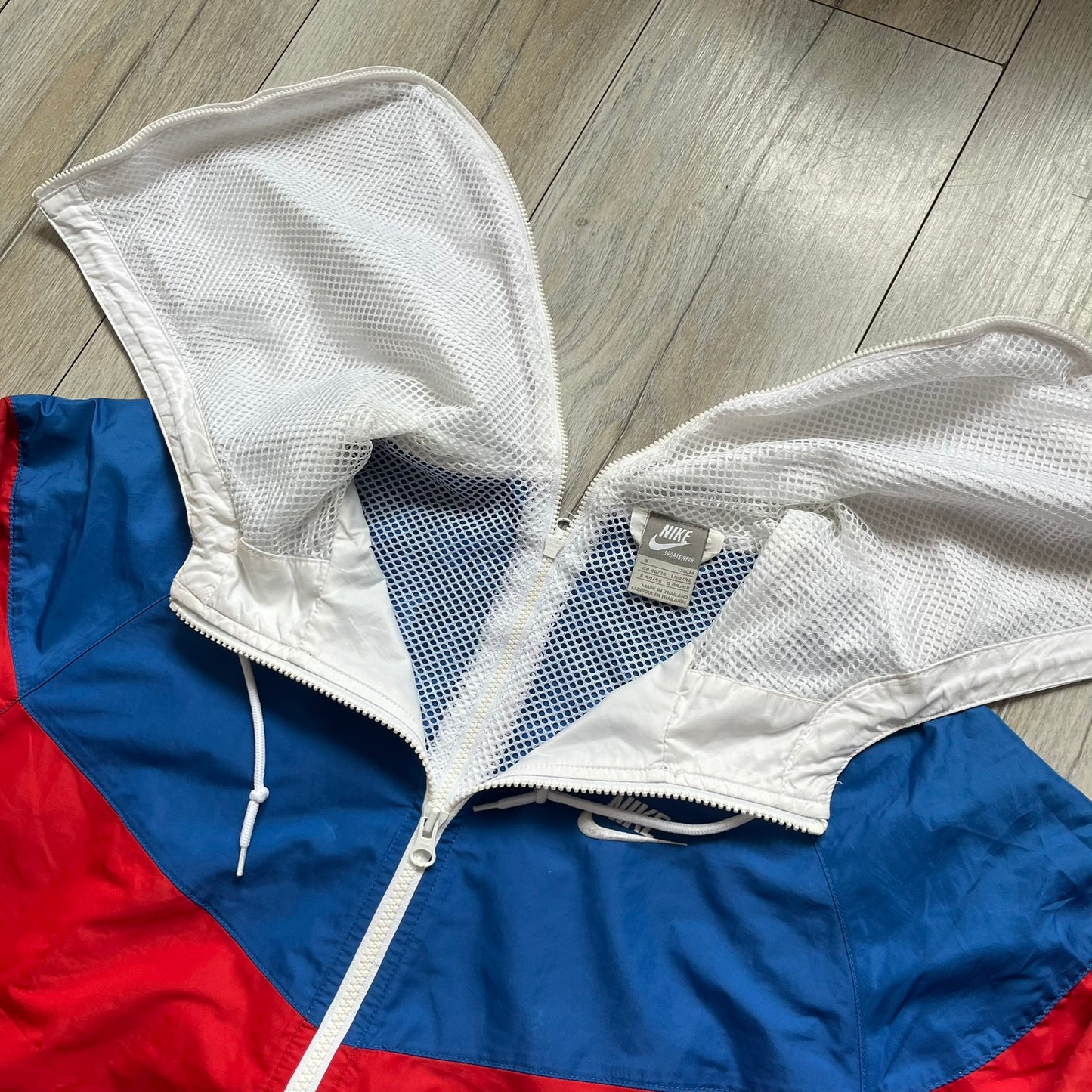 Nike Russia Olympics Split Windbreaker from 2008, created by designer Jarrett Reynolds. Crafted in a red, blue and white color wave. White Nike embroidery swoosh on the left side of the chest. The upper half of the jacket is blue with white hood, and the bottom is red with white accents. This innovative jacket can be zipped apart on both sides and merged with other compatible models. Hidden inside, a small Russia flags accent completes the concept.