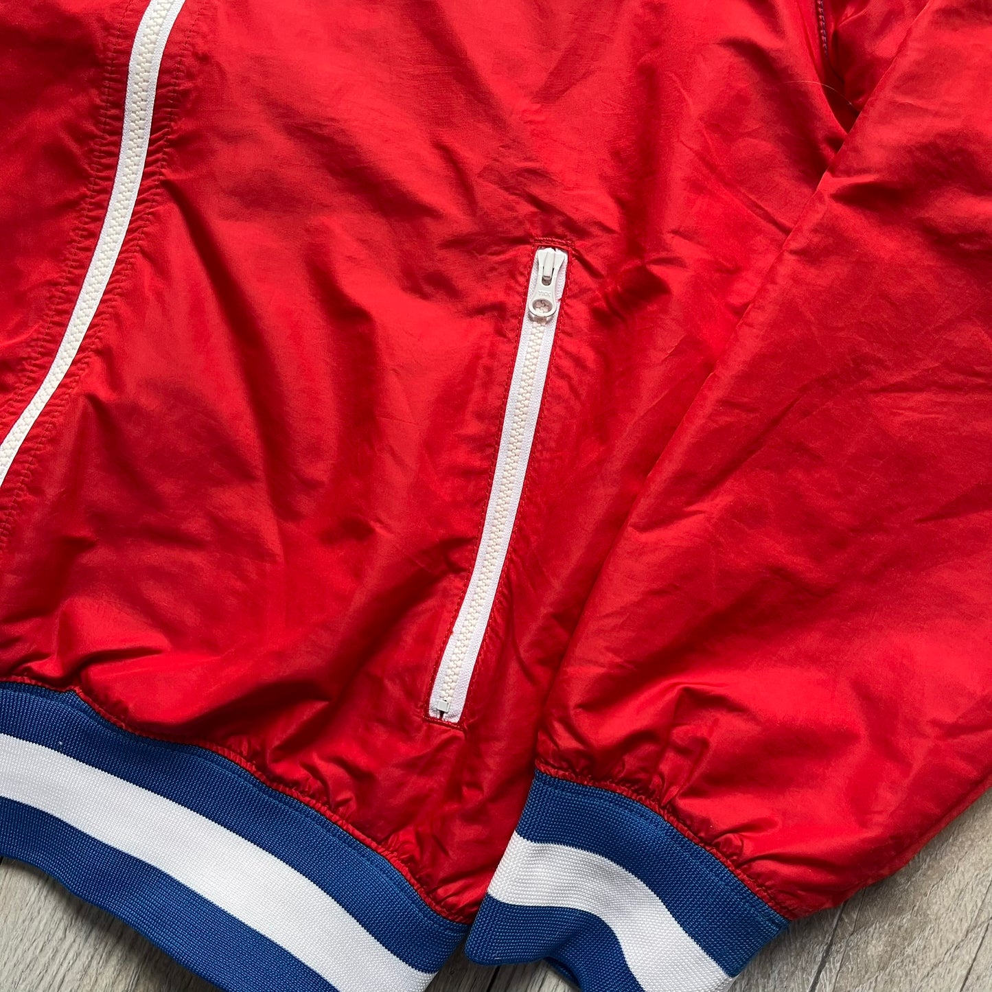 Nike Russia Olympics Split Windbreaker from 2008, created by designer Jarrett Reynolds. Crafted in a red, blue and white color wave. White Nike embroidery swoosh on the left side of the chest. The upper half of the jacket is blue with white hood, and the bottom is red with white accents. This innovative jacket can be zipped apart on both sides and merged with other compatible models. Hidden inside, a small Russia flags accent completes the concept.