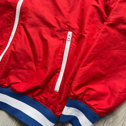 Nike Russia Olympics Split Windbreaker from 2008, created by designer Jarrett Reynolds. Crafted in a red, blue and white color wave. White Nike embroidery swoosh on the left side of the chest. The upper half of the jacket is blue with white hood, and the bottom is red with white accents. This innovative jacket can be zipped apart on both sides and merged with other compatible models. Hidden inside, a small Russia flags accent completes the concept.