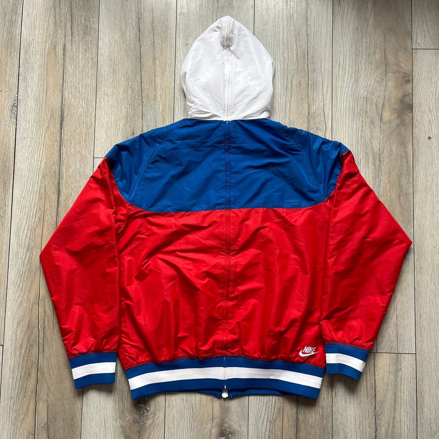 Nike Russia Olympics Split Windbreaker from 2008, created by designer Jarrett Reynolds. Crafted in a red, blue and white color wave. White Nike embroidery swoosh on the left side of the chest. The upper half of the jacket is blue with white hood, and the bottom is red with white accents. This innovative jacket can be zipped apart on both sides and merged with other compatible models. Hidden inside, a small Russia flags accent completes the concept.