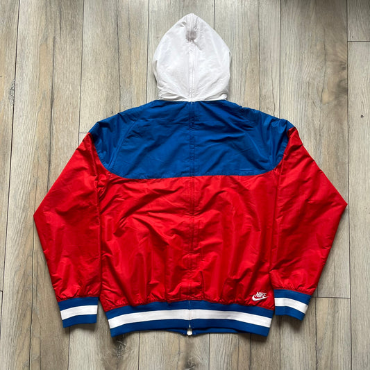 Nike Russia Olympics Split Windbreaker from 2008, created by designer Jarrett Reynolds. Crafted in a red, blue and white color wave. White Nike embroidery swoosh on the left side of the chest. The upper half of the jacket is blue with white hood, and the bottom is red with white accents. This innovative jacket can be zipped apart on both sides and merged with other compatible models. Hidden inside, a small Russia flags accent completes the concept.