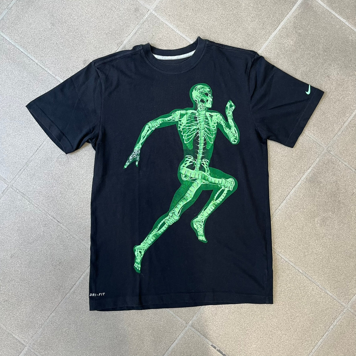 Nike SS11 "X-Ray Skeleton Free Faster" Tee is a black T-shirt from the Nike Free 2011 Spring/Summer season, designed by art director Kelvin Govey and designer Wonman Kim. The design features a large glow-in-the-dark green X-ray skeletal figure constructed entirely from parts of the Nike Free Run+2 shoe, with white Dri-FIT text at the bottom right and a green Nike Swoosh on the left sleeve.&nbsp;