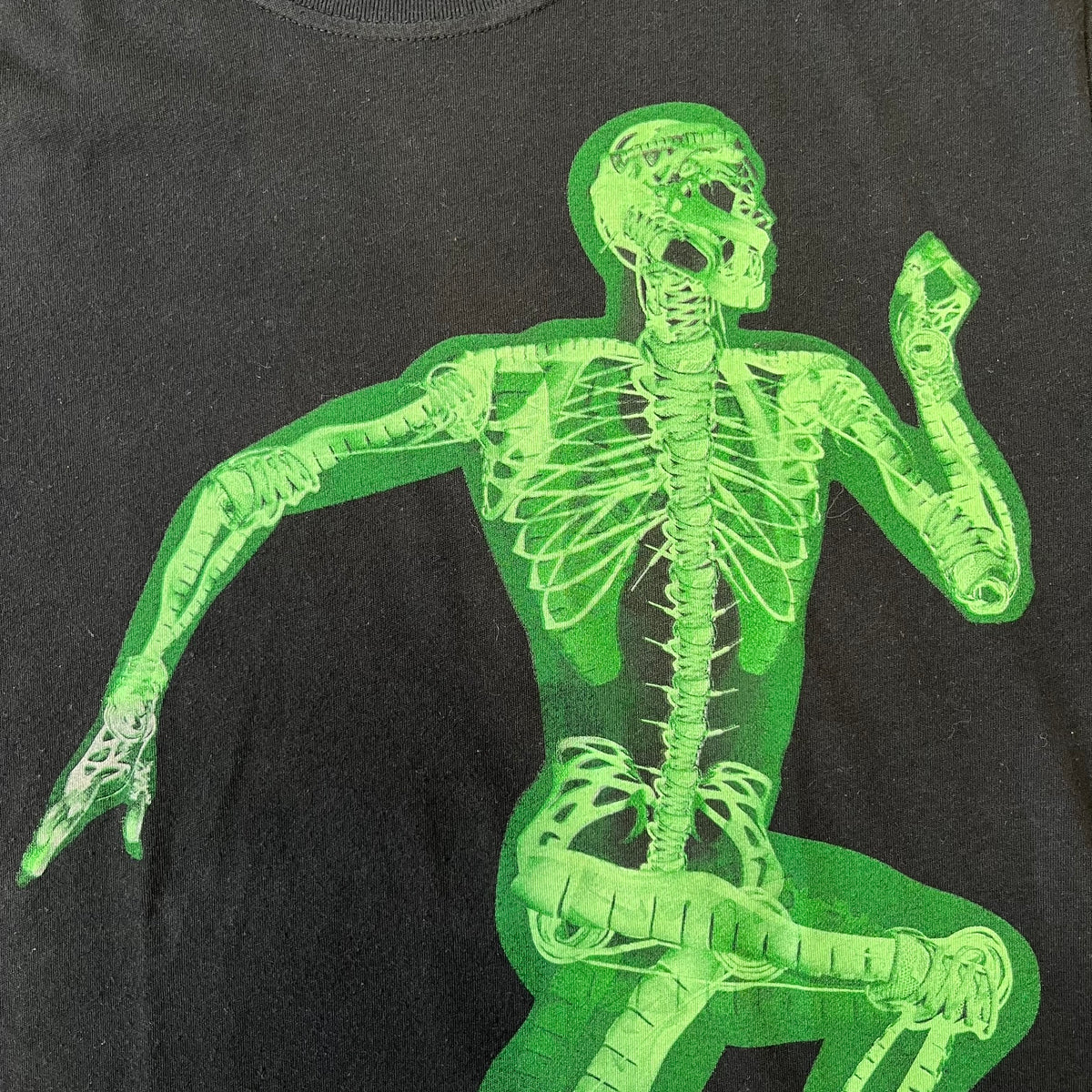 Nike SS11 "X-Ray Skeleton Free Faster" Tee is a black T-shirt from the Nike Free 2011 Spring/Summer season, designed by art director Kelvin Govey and designer Wonman Kim. The design features a large glow-in-the-dark green X-ray skeletal figure constructed entirely from parts of the Nike Free Run+2 shoe, with white Dri-FIT text at the bottom right and a green Nike Swoosh on the left sleeve.&nbsp;