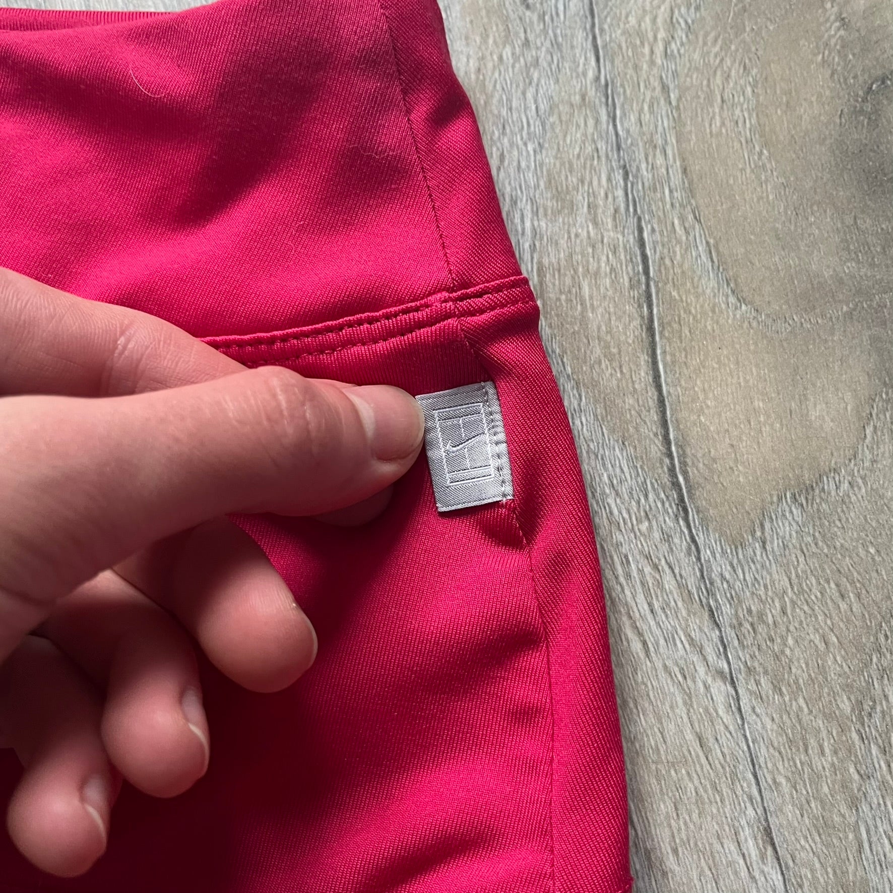 Nike Smash Classic Pink/Orange Tennis Skirt is a women’s tennis skort with built-in inner shorts. The design is constructed in three sections: a dark pink waistband and upper panel, an orange middle stripe, and a lower dark pink layer with two cutouts revealing orange fabric underneath. A white Nike Swoosh is placed at the lower hem, with a small Nike Court logo on the side.