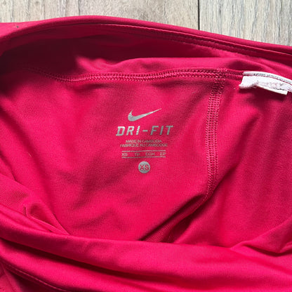 Nike Smash Classic Pink/Orange Tennis Skirt is a women’s tennis skort with built-in inner shorts. The design is constructed in three sections: a dark pink waistband and upper panel, an orange middle stripe, and a lower dark pink layer with two cutouts revealing orange fabric underneath. A white Nike Swoosh is placed at the lower hem, with a small Nike Court logo on the side.