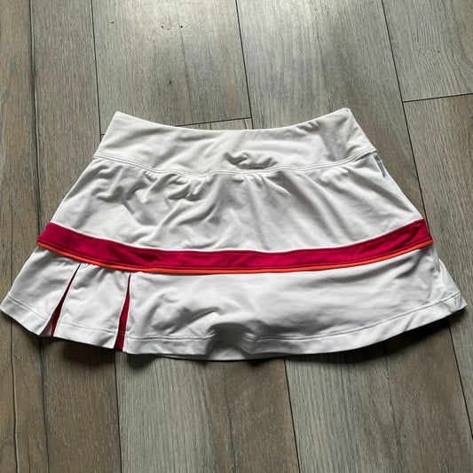 Nike Smash Classic White/Red Tennis Skirt is a women’s tennis skort with built-in inner shorts. The design is constructed in three sections: a white waistband and upper panel, a red middle stripe, and a lower white layer with two cutouts revealing red fabric underneath. A white Nike Swoosh is placed at the lower hem, with a small Nike Court logo on the side.