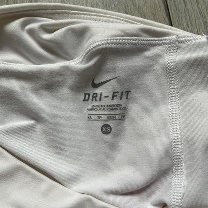 Nike Smash Classic White/Red Tennis Skirt is a women’s tennis skort with built-in inner shorts. The design is constructed in three sections: a white waistband and upper panel, a red middle stripe, and a lower white layer with two cutouts revealing red fabric underneath. A white Nike Swoosh is placed at the lower hem, with a small Nike Court logo on the side.