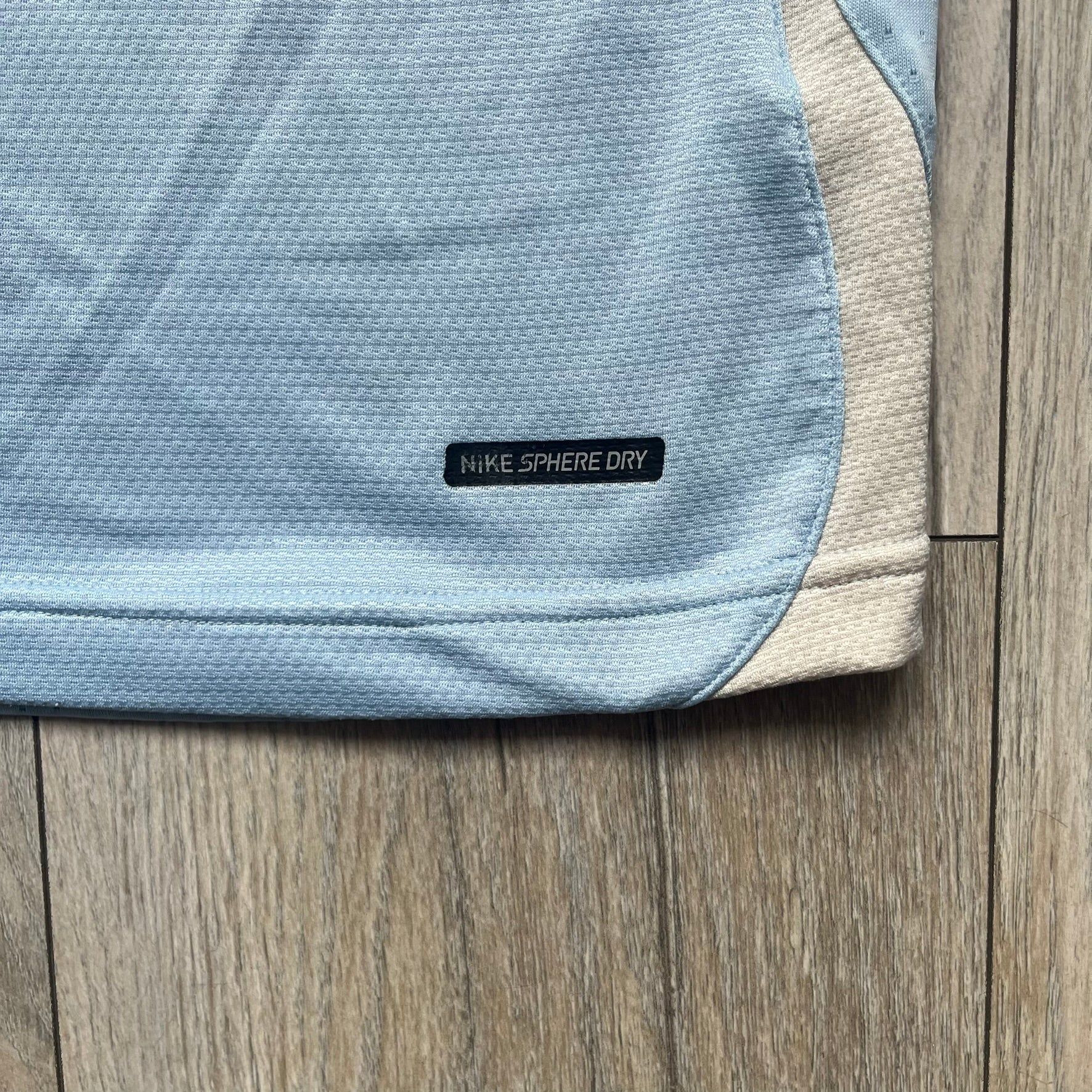 Nike Sphere Dry 90’s Baby Blue Tee is a baby blue T-shirt featuring gray and white stripe detailing. The front includes a dark gray Nike logo alongside a “90” graphic, with an additional Nike logo on the sleeve. The back displays a large light blue “90” print