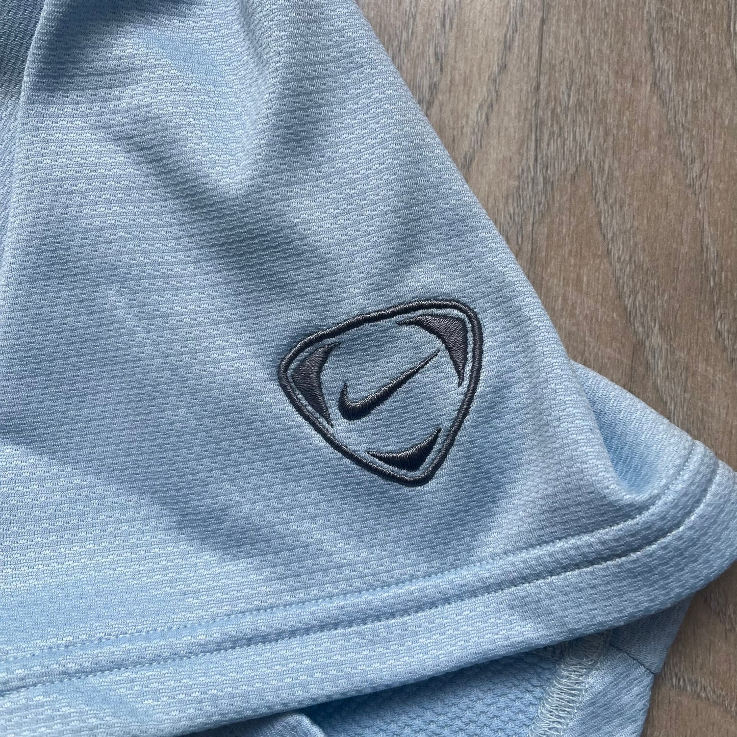 Nike Sphere Dry 90’s Baby Blue Tee is a baby blue T-shirt featuring gray and white stripe detailing. The front includes a dark gray Nike logo alongside a “90” graphic, with an additional Nike logo on the sleeve. The back displays a large light blue “90” print