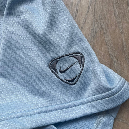 Nike Sphere Dry 90’s Baby Blue Tee is a baby blue T-shirt featuring gray and white stripe detailing. The front includes a dark gray Nike logo alongside a “90” graphic, with an additional Nike logo on the sleeve. The back displays a large light blue “90” print