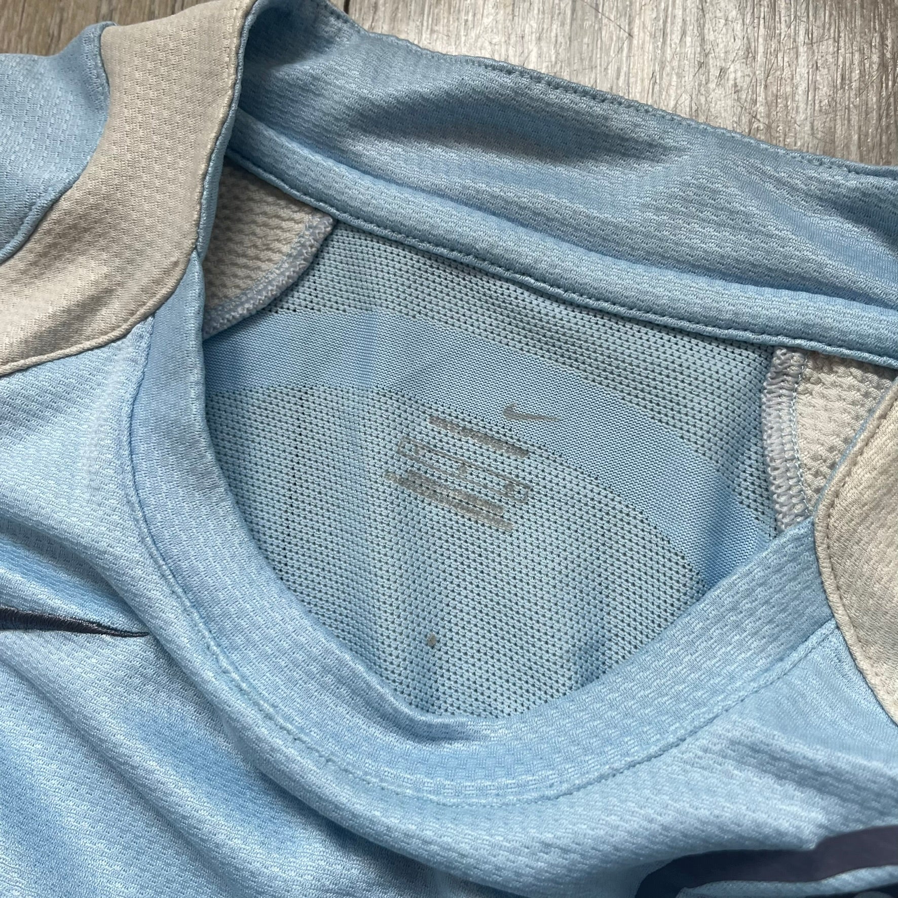 Nike Sphere Dry 90’s Baby Blue Tee is a baby blue T-shirt featuring gray and white stripe detailing. The front includes a dark gray Nike logo alongside a “90” graphic, with an additional Nike logo on the sleeve. The back displays a large light blue “90” print