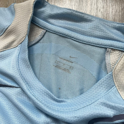 Nike Sphere Dry 90’s Baby Blue Tee is a baby blue T-shirt featuring gray and white stripe detailing. The front includes a dark gray Nike logo alongside a “90” graphic, with an additional Nike logo on the sleeve. The back displays a large light blue “90” print
