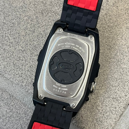 Nike Steelhead 2000’s Sport Chrono VG02-5000 Watch has a gray and black checkered analog dial with red hands, set in a rounded triangle shape. Below it is a small digital screen made of three connected circles. The case is black and silver with a red Nike Swoosh at the bottom, and the original straps have been replaced with basic non-Nike rubber ones.