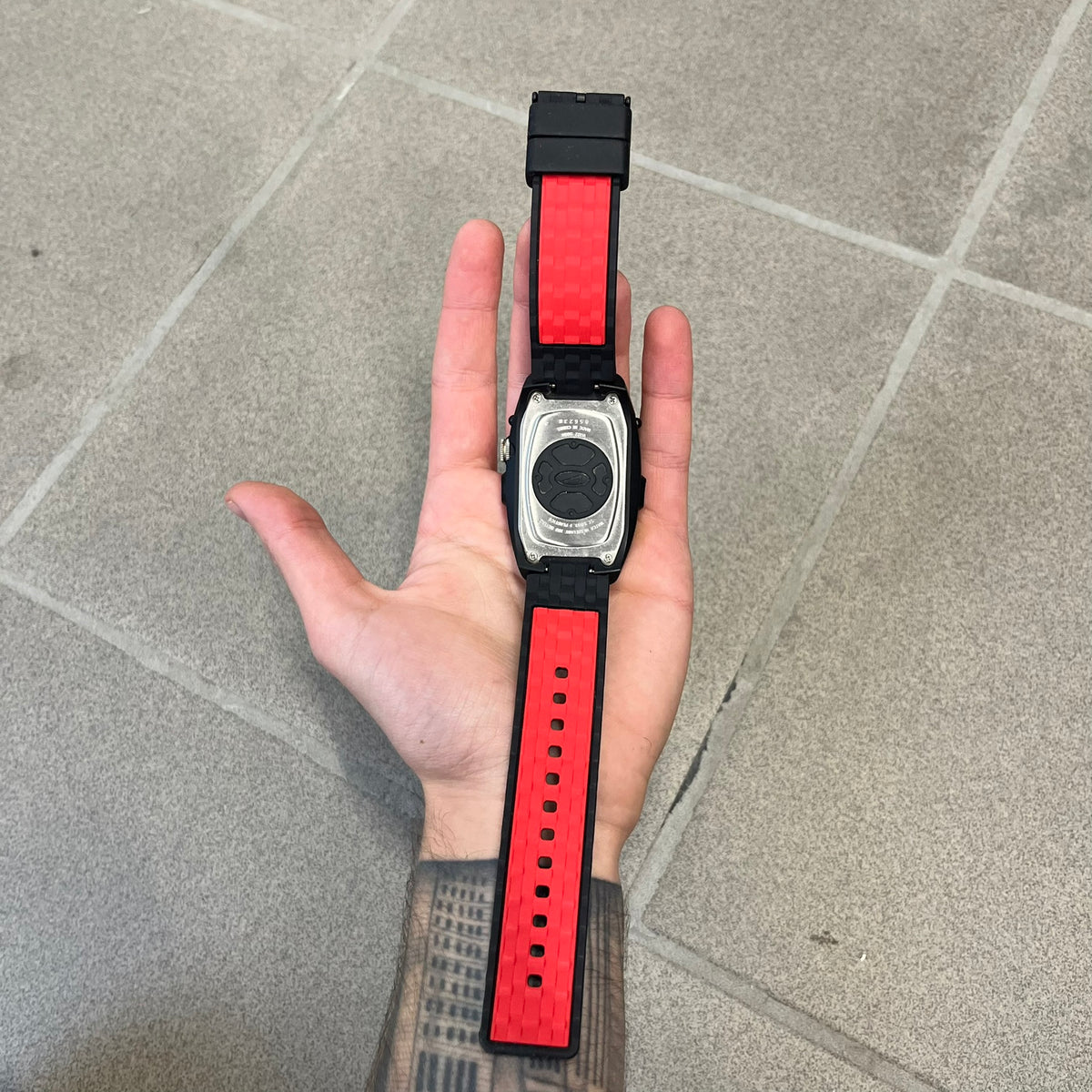 Nike Steelhead 2000’s Sport Chrono VG02-5000 Watch has a gray and black checkered analog dial with red hands, set in a rounded triangle shape. Below it is a small digital screen made of three connected circles. The case is black and silver with a red Nike Swoosh at the bottom, and the original straps have been replaced with basic non-Nike rubber ones.