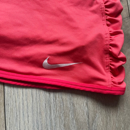 Nike Tie Break Knit 2012 Coral Tennis Skirt is a women’s tennis skort in coral featuring an integrated inner shorts layer. The skirt has a flared, creased design at the sides and a white Nike Swoosh at the lower hem. Designed for sporty performance, it combines lightweight knit construction with Nike’s 2012 Tie Break tennis line styling.