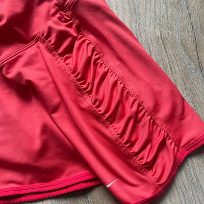 Nike Tie Break Knit 2012 Coral Tennis Skirt is a women’s tennis skort in coral featuring an integrated inner shorts layer. The skirt has a flared, creased design at the sides and a white Nike Swoosh at the lower hem. Designed for sporty performance, it combines lightweight knit construction with Nike’s 2012 Tie Break tennis line styling.