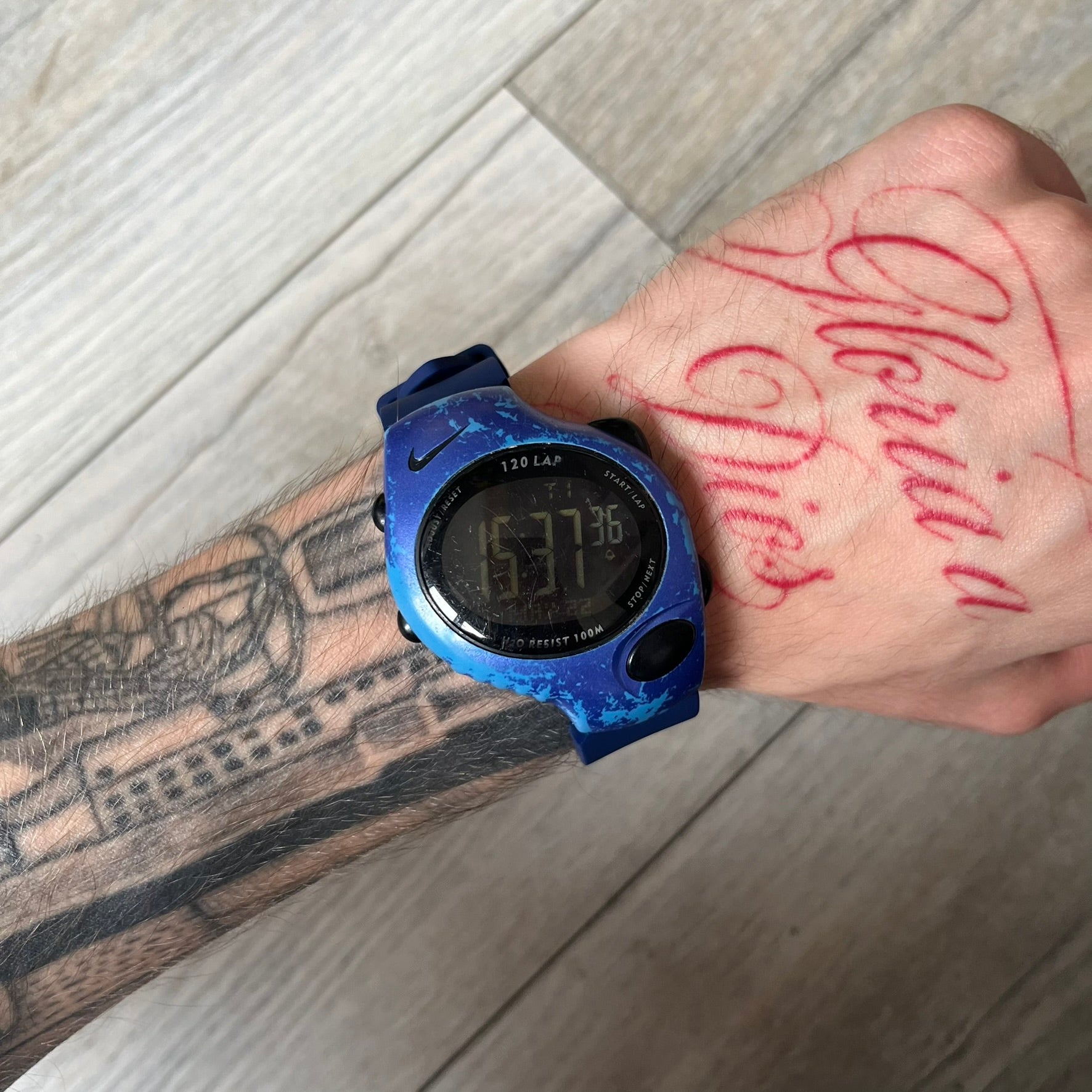 Nike Triax 120 WG40-0010 Digital Watch features a blue case with a black Nike Swoosh above the display and a black control button below it. The watch has a black digital screen with light-colored numerals and is fitted with navy-blue replacement straps that are not original Nike straps. Constructed from stainless steel and plastic materials, it offers 100-meter water resistance, 120-lap memory, and multiple timing and training modes.