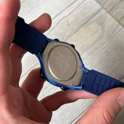 Nike Triax 120 WG40-0010 Digital Watch features a blue case with a black Nike Swoosh above the display and a black control button below it. The watch has a black digital screen with light-colored numerals and is fitted with navy-blue replacement straps that are not original Nike straps. Constructed from stainless steel and plastic materials, it offers 100-meter water resistance, 120-lap memory, and multiple timing and training modes.
