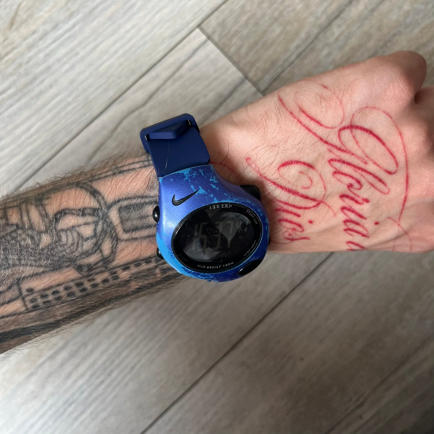 Nike Triax 120 WG40-0010 Digital Watch features a blue case with a black Nike Swoosh above the display and a black control button below it. The watch has a black digital screen with light-colored numerals and is fitted with navy-blue replacement straps that are not original Nike straps. Constructed from stainless steel and plastic materials, it offers 100-meter water resistance, 120-lap memory, and multiple timing and training modes.