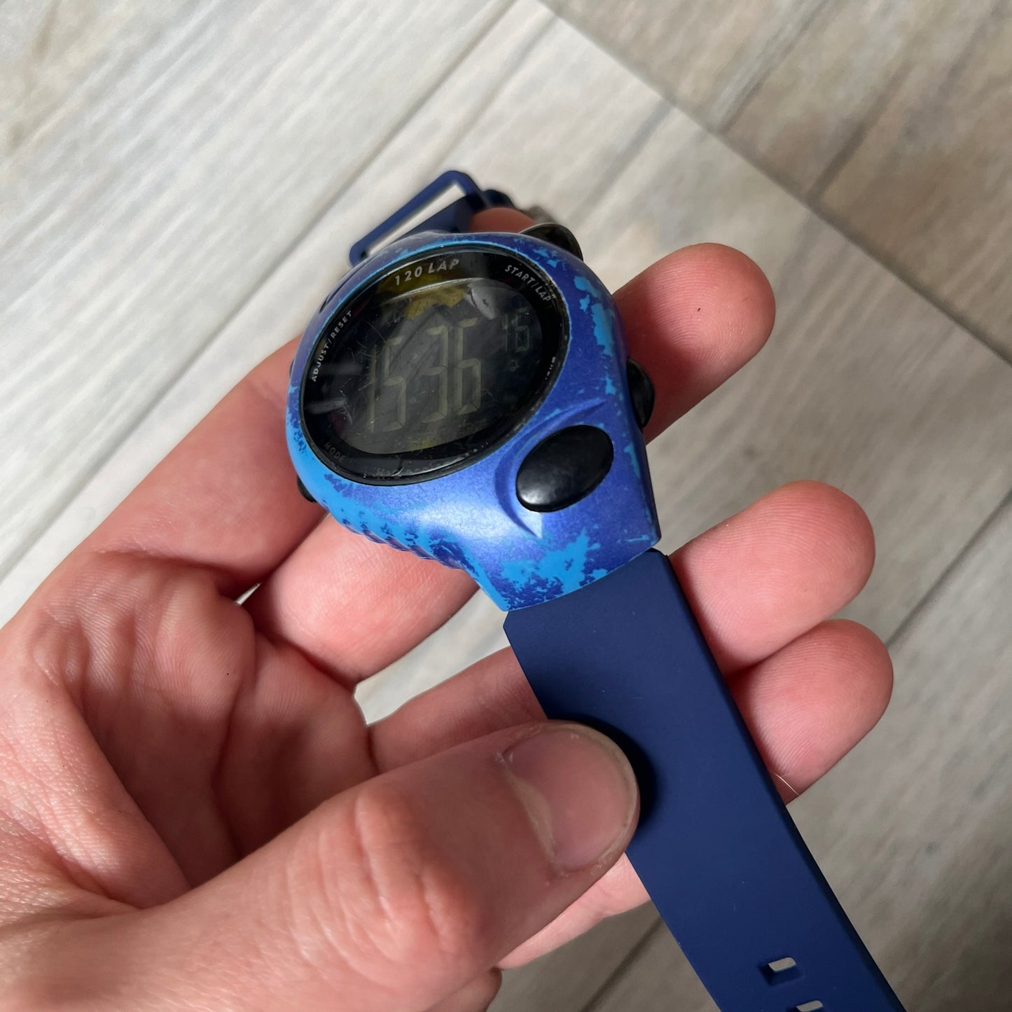 Nike Triax 120 WG40-0010 Digital Watch features a blue case with a black Nike Swoosh above the display and a black control button below it. The watch has a black digital screen with light-colored numerals and is fitted with navy-blue replacement straps that are not original Nike straps. Constructed from stainless steel and plastic materials, it offers 100-meter water resistance, 120-lap memory, and multiple timing and training modes.