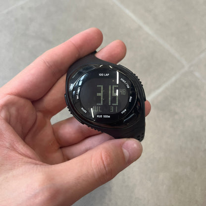 Nike Triax 2000's Bowerman Black Speed 100 Digital Watch features an all-black construction with rubber straps and a black digital display with light numerals. The case has a small Nike Swoosh at the top, while the watch includes 100-lap memory, multiple modes, and 100m water resistance.