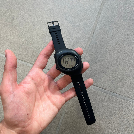 Nike Triax 2000's Super 10 Lap Digital Watch features a black case with a small white Nike Swoosh above the digital display. It has 10-lap memory, four modes, a light-up display, and water resistance. Model WR0005-001. The rubber straps have been replaced with non-original ones.
