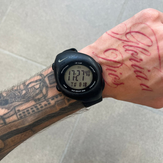 Nike Triax 2000's Super 10 Lap Digital Watch features a black case with a small white Nike Swoosh above the digital display. It has 10-lap memory, four modes, a light-up display, and water resistance. Model WR0005-001. The rubber straps have been replaced with non-original ones.
