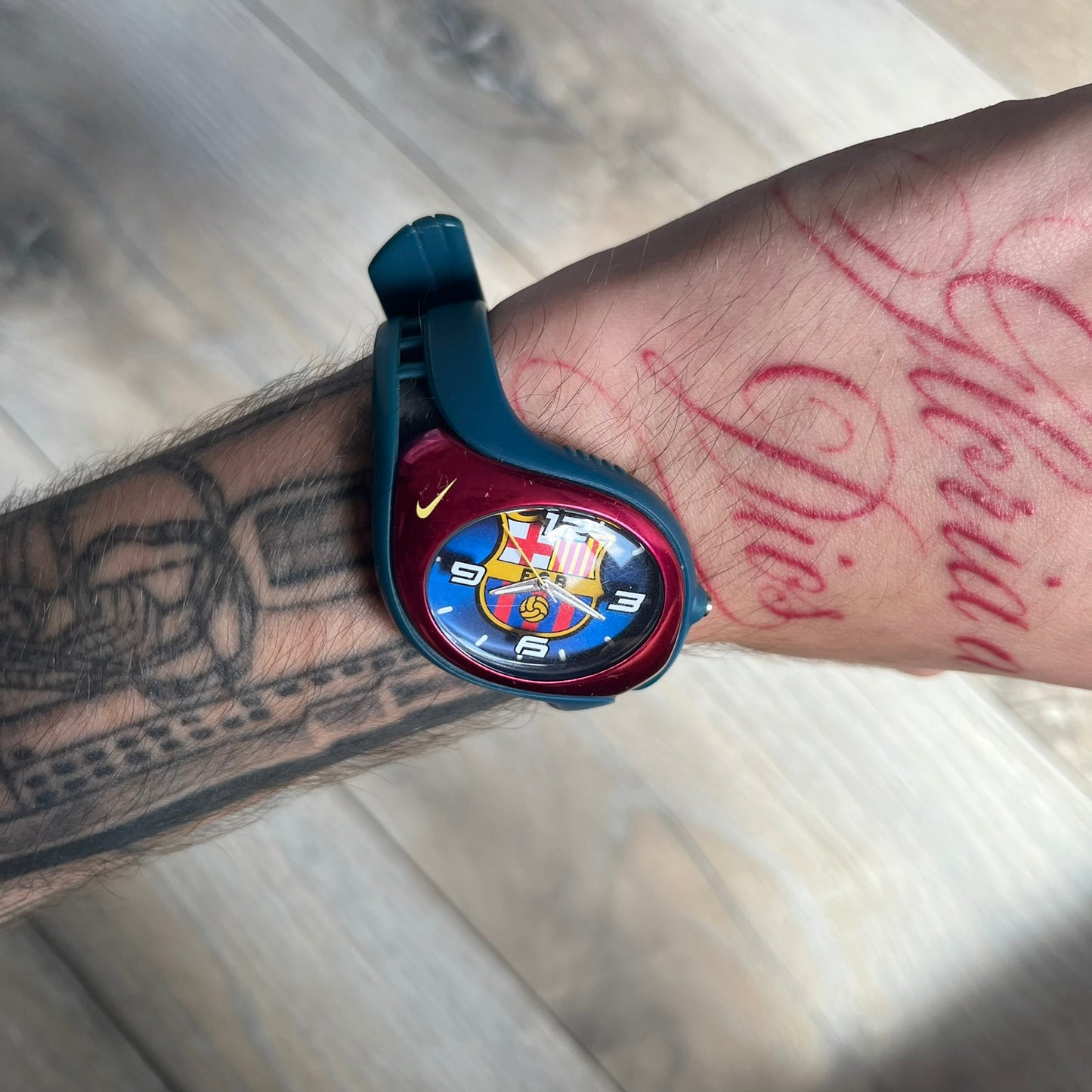 Nike Triax 2005 FC Barcelona WK0008 Analog Watch is a vintage watch featuring a navy rubber strap, red plastic case, and navy dial. The dial displays a large full-color FC Barcelona crest with white numerals, while a yellow Nike Swoosh is positioned at the top of the case. The watch is water resistant up to 50 meters and is constructed from stainless steel and plastic materials.