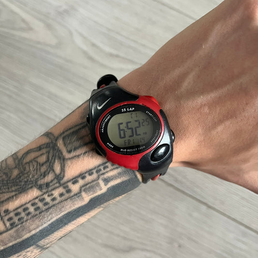 Digital watch with red and black strap on a wrist with tattoos