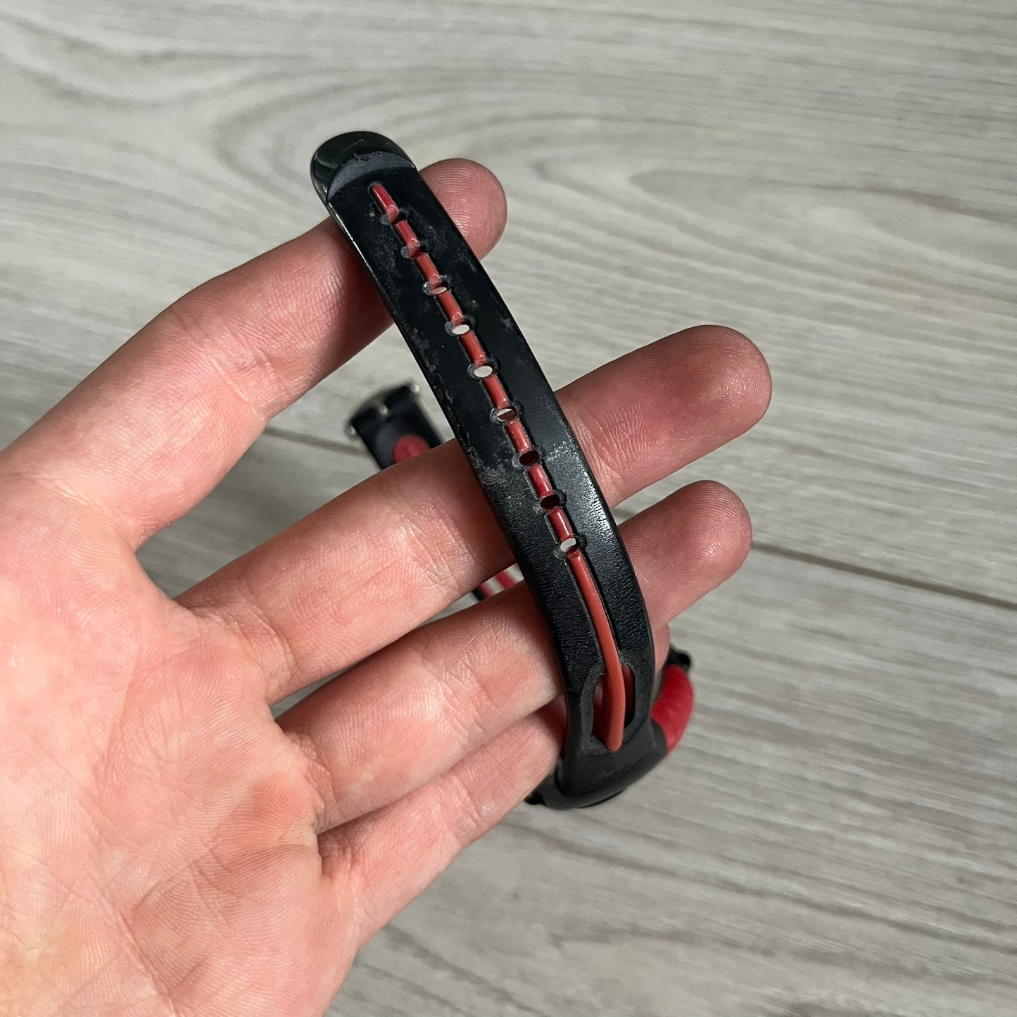 Hand holding a black and red leather bracelet against a light wooden background