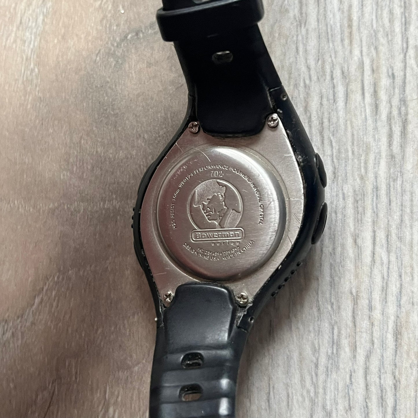 The Nike Triax Bowerman WR0124 Black Digital Watch features black rubber straps and a black plastic case with a metal caseback engraved with the Bowerman logo. It includes a digital display with multiple modes, a 10-lap memory function, H2O 100 water resistance, and a built-in backlight. The watch has a single front button and a white Nike logo on the case.