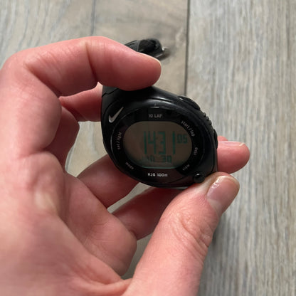 The Nike Triax Bowerman WR0124 Black Digital Watch features black rubber straps and a black plastic case with a metal caseback engraved with the Bowerman logo. It includes a digital display with multiple modes, a 10-lap memory function, H2O 100 water resistance, and a built-in backlight. The watch has a single front button and a white Nike logo on the case.