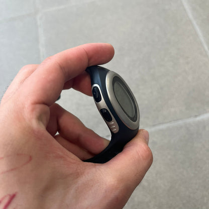 Nike Triax Elite SM0019 Digital Watch features a large asymmetrical silver-tone case with navy rubber case and straps integrated into the case. The top of the case is detailed with a Nike Swoosh, while the front includes Triax Elite branding. The watch has five side buttons, a digital display with multiple functions, and 100-lap memory. It comes with an untested Nike heart rate monitor (HRM) device and an original Nike watch display stand.