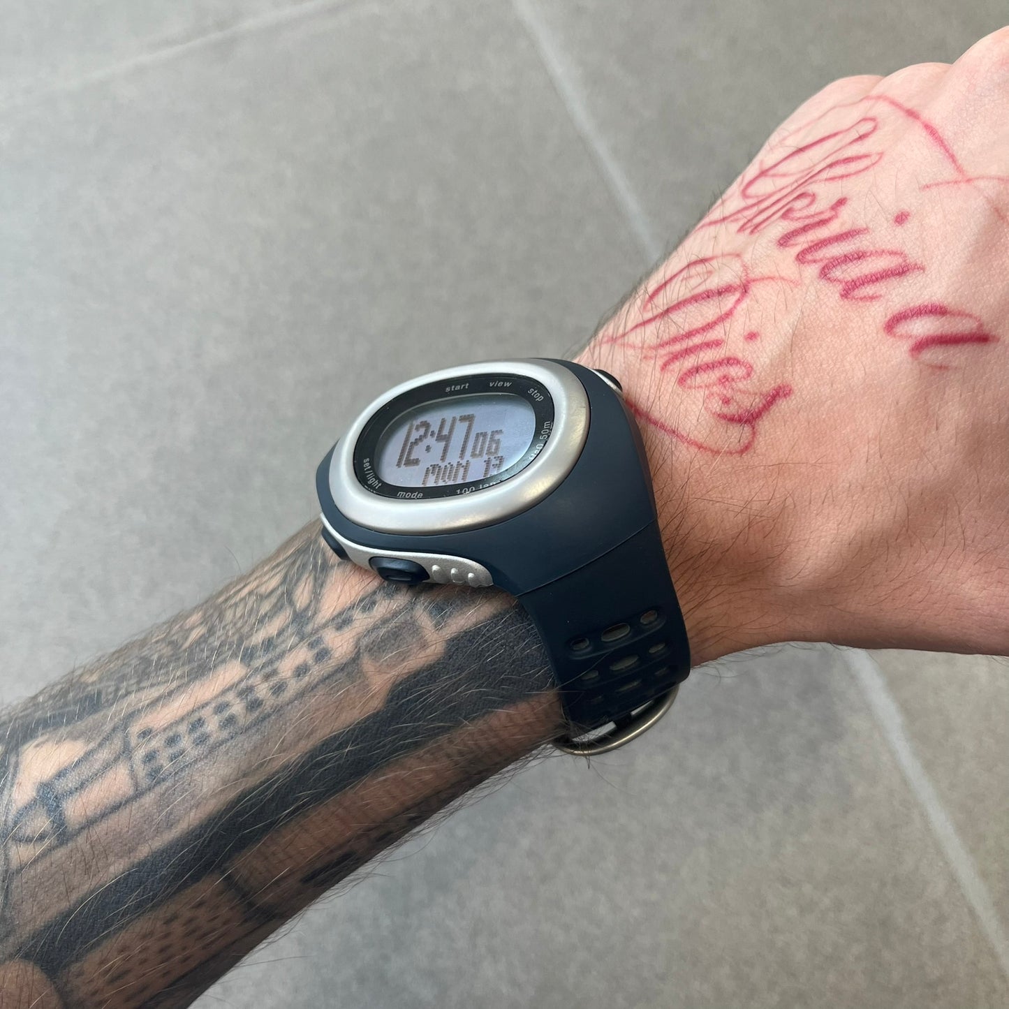 Nike Triax Elite SM0019 Digital Watch features a large asymmetrical silver-tone case with navy rubber case and straps integrated into the case. The top of the case is detailed with a Nike Swoosh, while the front includes Triax Elite branding. The watch has five side buttons, a digital display with multiple functions, and 100-lap memory. It comes with an untested Nike heart rate monitor (HRM) device and an original Nike watch display stand.