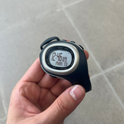 Nike Triax Elite SM0019 Digital Watch features a large asymmetrical silver-tone case with navy rubber case and straps integrated into the case. The top of the case is detailed with a Nike Swoosh, while the front includes Triax Elite branding. The watch has five side buttons, a digital display with multiple functions, and 100-lap memory. It comes with an untested Nike heart rate monitor (HRM) device and an original Nike watch display stand.